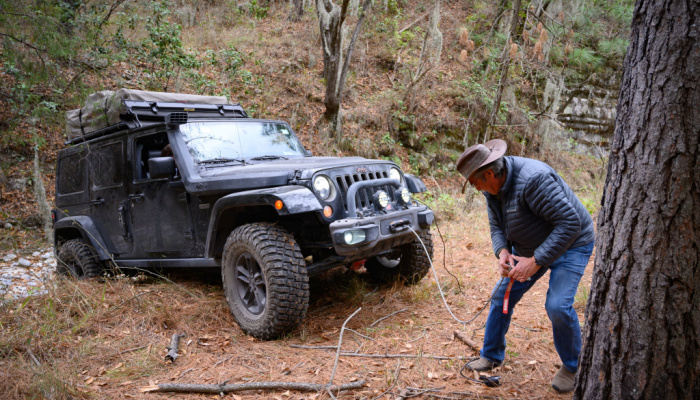 A man with a cowboy hat helping to climb an obstacle a jeep with the vehicle winch