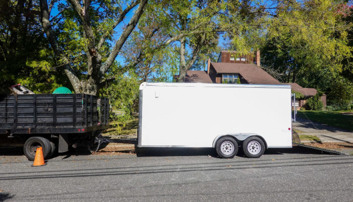A truck with a long white enclosed trailer and a hitch on a shady residential asphalt street