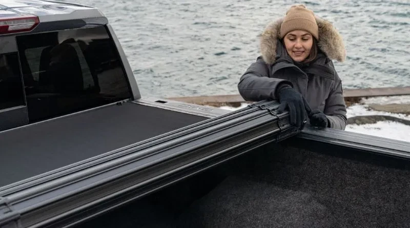 woman on a winter jacket rolling up a roll up truck bed cover