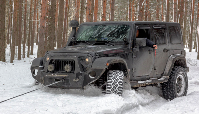 Jeep Wrangler with a driver inside in a winter forest stuck in snow